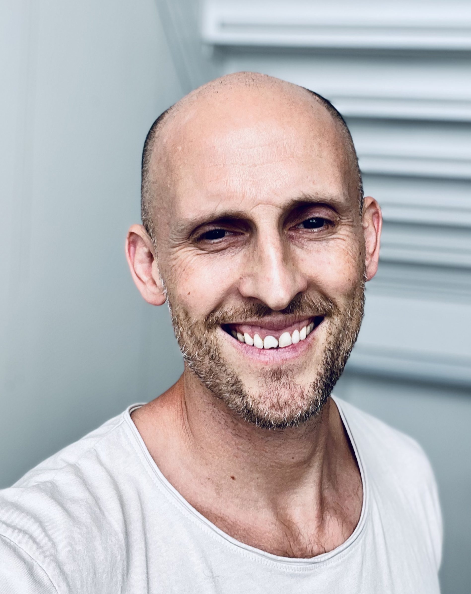 handheld selfie picture of a man wearing a off white T-shirt indoors. bright natural lighting