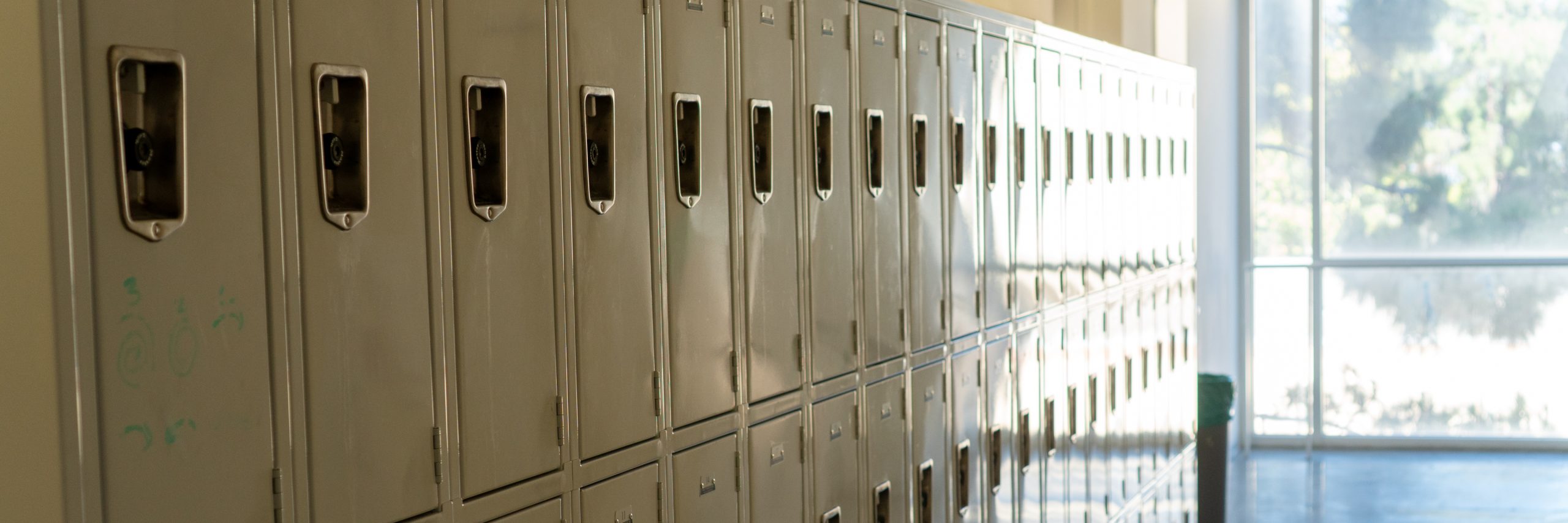 An interior shot of a hallway with stacked lockers taking up most of the view. Light comes in through window in the background.