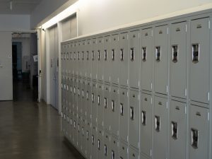 An interior photo of a stacked row of lockers occuping the foreground. Three doors are in the background, one of them is open.